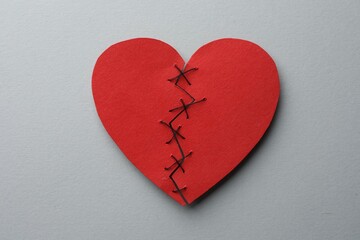 Broken heart. Torn red paper heart sewed with thread on light grey background, top view
