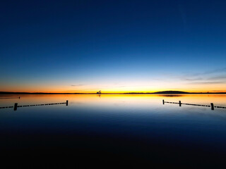 Sunset at Lake Störmthal. Sun creates thin yellow to red light streaks on the horizon. the rest of the picture is deep blue. Unique atmosphere on a lake near Leipzig.