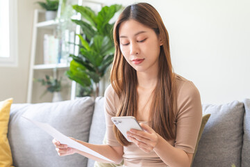 Smiling young woman calculate finances, hand holding mobile phone and invoice paper pay from bills tax, online bill payment transactions from app via smartphone, using banking service in internet.