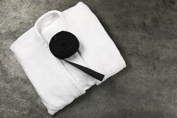 Black karate belt and white kimono on gray textured background, top view. Space for text