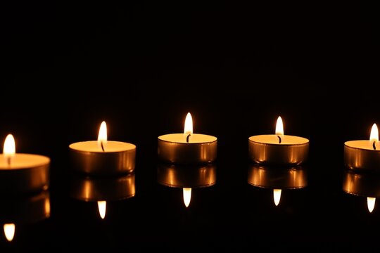 Burning candles on mirror surface in darkness
