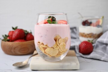 Glass with yogurt, strawberries and corn flakes on white textured table