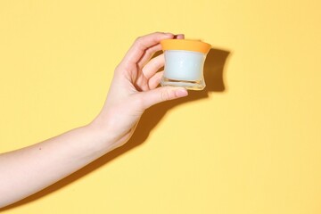 Woman holding jar of cream on yellow background, closeup
