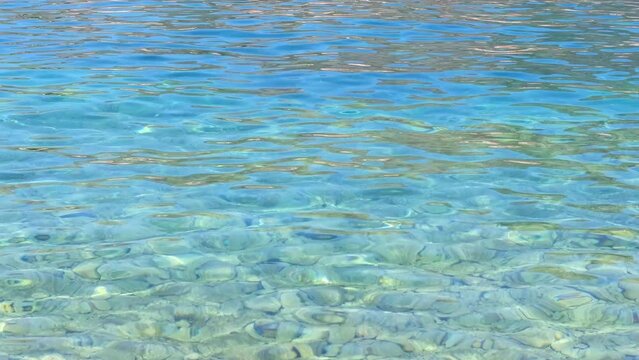 Crystal clear and transparent turquoise blue sea water washes over the pebbles on the seabed. The water glistens and shimmers in the sun. Concept of tourism, sea, summer holiday. Copy space