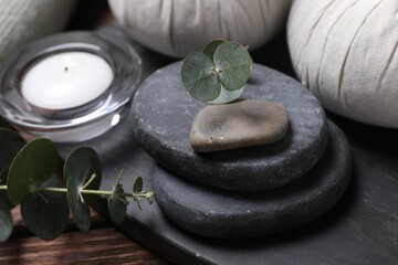 Beautiful spa composition with herbal massage bags, stones and eucalyptus branches on wooden table, closeup