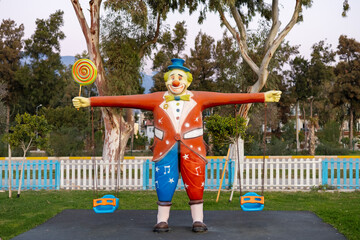Joyful statue of a clown with outstretched arms from which a swing hangs in the park