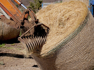A mechanical rake and fork arm moves and unloads a bale of hay from a truck - 759813866