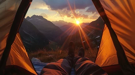 Tuinposter View from tent to sunset in mountains. Legs on blanket with sleeping bags on mountain hill © lelechka