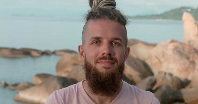 Beach setting man's confident look into camera rocks with sea at background. Confidence interwoven with tranquility Confidence foundation for mental well-being Confidence unlocking joy of living.