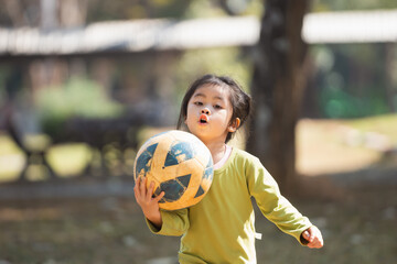 A young girl is holding a soccer ball in her hands. She is wearing a green shirt and she is excited...
