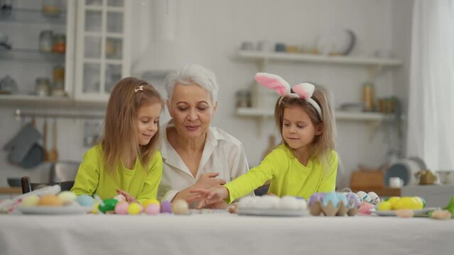 Easter grandmothers with granddaughters. Smiling grandmother with twins grandchildren painting decorating eggs in rabbit bunny ears, celebrate holiday at home. Easter family holiday concept.