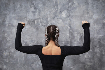 An athletic woman is training near a wall, stands with her back to the camera, bends her arms at a...
