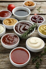 Different tasty sauces in bowls, rosemary and thyme on wooden table