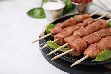 Wooden skewers with cut raw marinated meat on white tiled table, closeup. Space for text
