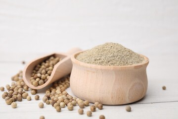 Aromatic spice. Ground pepper in bowl and scoop with peppercorns on white wooden table, closeup