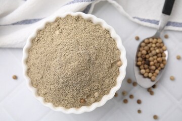 Ground pepper and peppercorns on white tiled table, top view