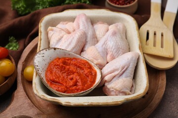 Fresh marinade, raw chicken and tomatoes on brown table, closeup