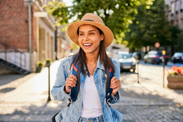 Portrait of happy female tourist walking on city street with backpack during summer city break