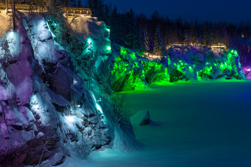 The steep wall of the Marble Canyon in multi-colored illumination on a January night. Ruskeala Mountain Park. Karelia, Russia
