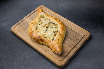 Khachapuri with cheese and mushrooms on a wooden cutting board
