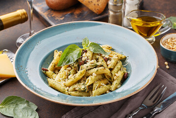 Pasta penne with chicken, pine nuts, beans, pesto sauce and basil leaves on dark concrete background. Side view, close up, selective focus