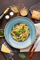 Pasta penne with chicken, pine nuts, beans, pesto sauce and basil leaves on dark concrete background. Overhead view, flat lay