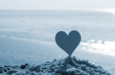Plastic stick in shape of red heart in sand on sandy beach of sea shore on sea waves on sunny...