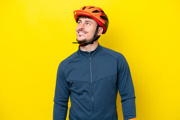 Young cyclist caucasian man isolated on yellow background thinking an idea while looking up