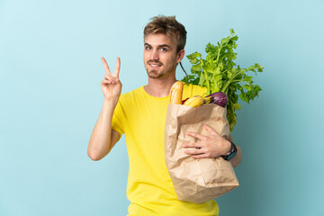 blonde Person taking a bag of takeaway food isolated on blue background smiling and showing victory...