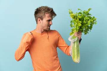 Young blonde man holding a celery isolated on blue background celebrating a victory