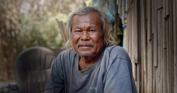 A smiling Asian man who is a homeless ragpicker or has a career collecting garbage and selling it, live in a abandoned house at a slum village.