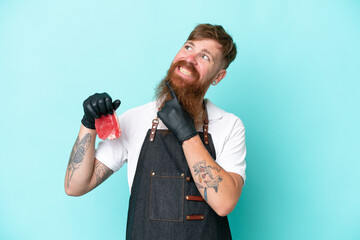 Butcher man wearing an apron and serving fresh cut meat isolated on blue background looking up...