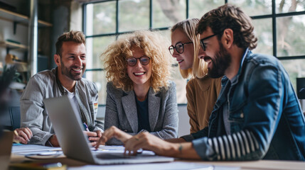 Colleagues are in a collaborative office setting, all smiling and engaged in a discussion with laptops open in front of them.