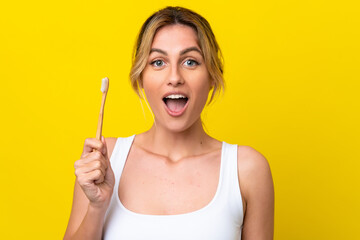 Young Uruguayan woman brushing teeth isolated on yellow background with surprise and shocked facial...