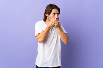 Young handsome man isolated on purple background covering mouth and looking to the side