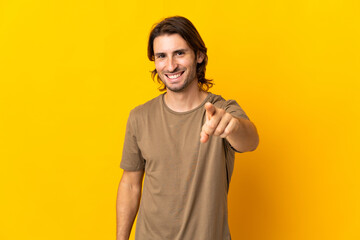 Young handsome man isolated on yellow background surprised and pointing front
