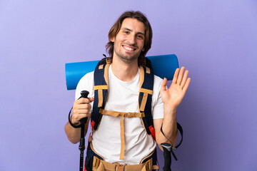 Young mountaineer man with a big backpack over isolated background saluting with hand with happy expression