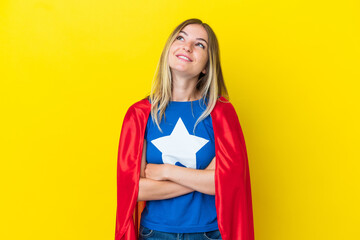 Super Hero Romanian woman isolated on yellow background looking up while smiling