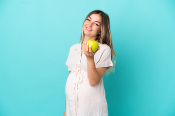 Young Romanian woman isolated on blue background pregnant and holding an apple