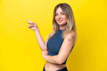 Young Rumanian woman isolated on yellow background pointing finger to the side