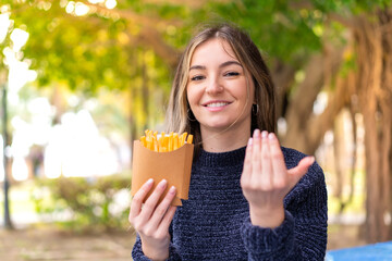 Young pretty Romanian woman holding fried chips at outdoors inviting to come with hand. Happy that you came