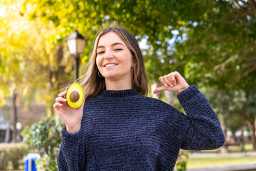 Young pretty Romanian woman holding an avocado at outdoors proud and self-satisfied