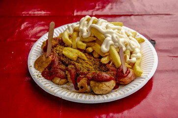A typical Berlin snack: currywurst and pommes with mayonaise on a wooden plate on a red table cloth
