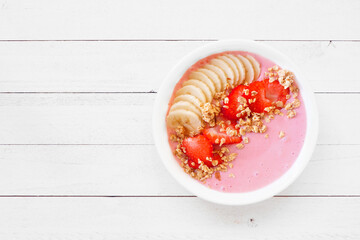 Healthy strawberry and banana smoothie bowl with granola. Top view on a white wood background.