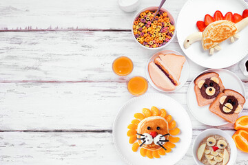Fun child theme breakfast side border with a variety of animal themed food. Top down view on a white wood background. Pancakes, oatmeal, toast, fruit and cereal. - 759896467