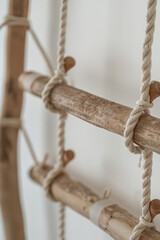 Minimalist Wooden Wall Ladder. Close-up of minimalist wall ladder with wooden rungs secured by rope, sports complex for children's room, white background.