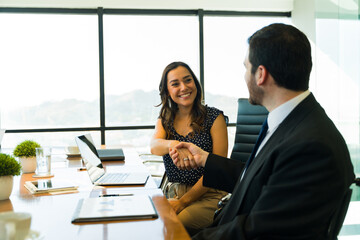 Latin woman striking a deal with a client and shaking hands in a meeting room