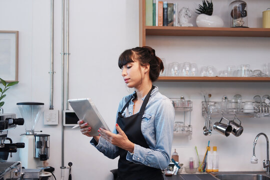 Smiling Caucasian Young barista woman is wearing apron and writing online order and menu of customers on tablet in cafe and coffee shop. Start up small cafe business and technology Concept