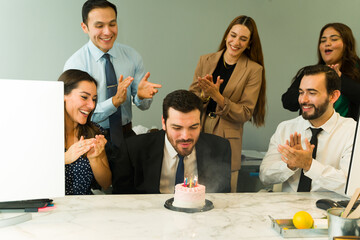 Businessman blowing off the candles of a birthday cake he just got from his coworkers