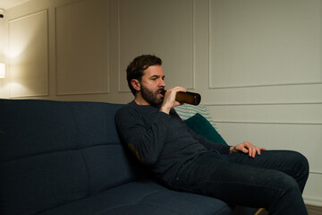 Upset lonely man drinking beer late at night in the living room